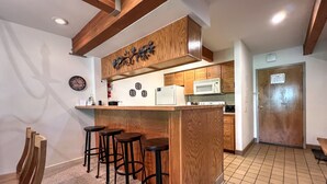 A kitchen with wooden cabinets, a microwave, a refrigerator, and a wooden island with bar stools. - Comfortable Condo close to Slopes with a Hot Tub! (Mt. Crested Butte)