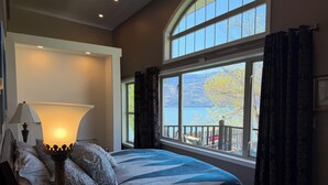 Une chambre à coucher avec un lit, une lampe, une fenêtre avec des rideaux et une vue sur un lac.