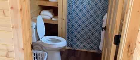 A small, wooden cabin bathroom with a toilet, shelves with towels, and a shower curtain.