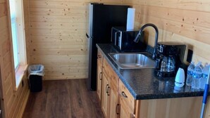Ett kompakt kök med träväggar, en diskho, ett kylskåp och en kaffebryggare.