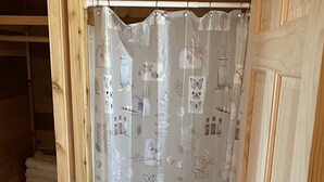 A bathroom with a shower curtain featuring botanical and butterfly designs, a toilet, and a wooden shelving unit with folded towels. - One Bedroom Cabin w/Sleeper Sofa Cabin 8 (Hamilton)