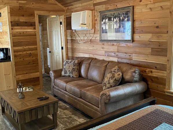 A wooden cabin interior with a brown leather sofa, a wooden coffee table, and a framed picture on the wall.