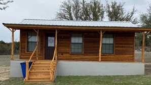 A wooden cabin with a porch, a front door, and a staircase leading to the entrance. - One Bedroom Cabin w/Sleeper Sofa Cabin 8 (Hamilton)