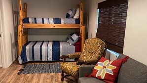 A compact living space with a bunk bed, a sofa, a patterned armchair, and a wooden floor. - On the Frio River (Leakey)