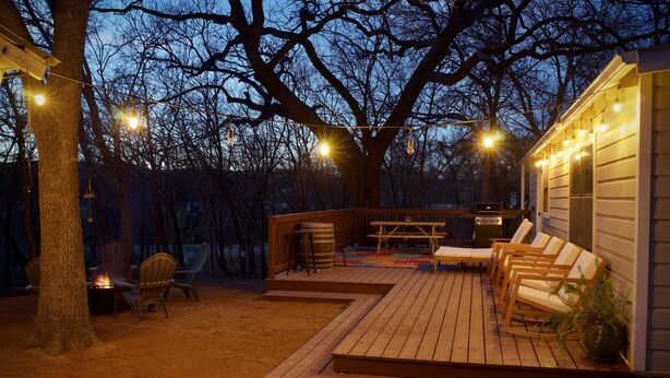 A wooden deck with outdoor furniture, a fire pit, and string lights. - On the Frio River (Leakey)
