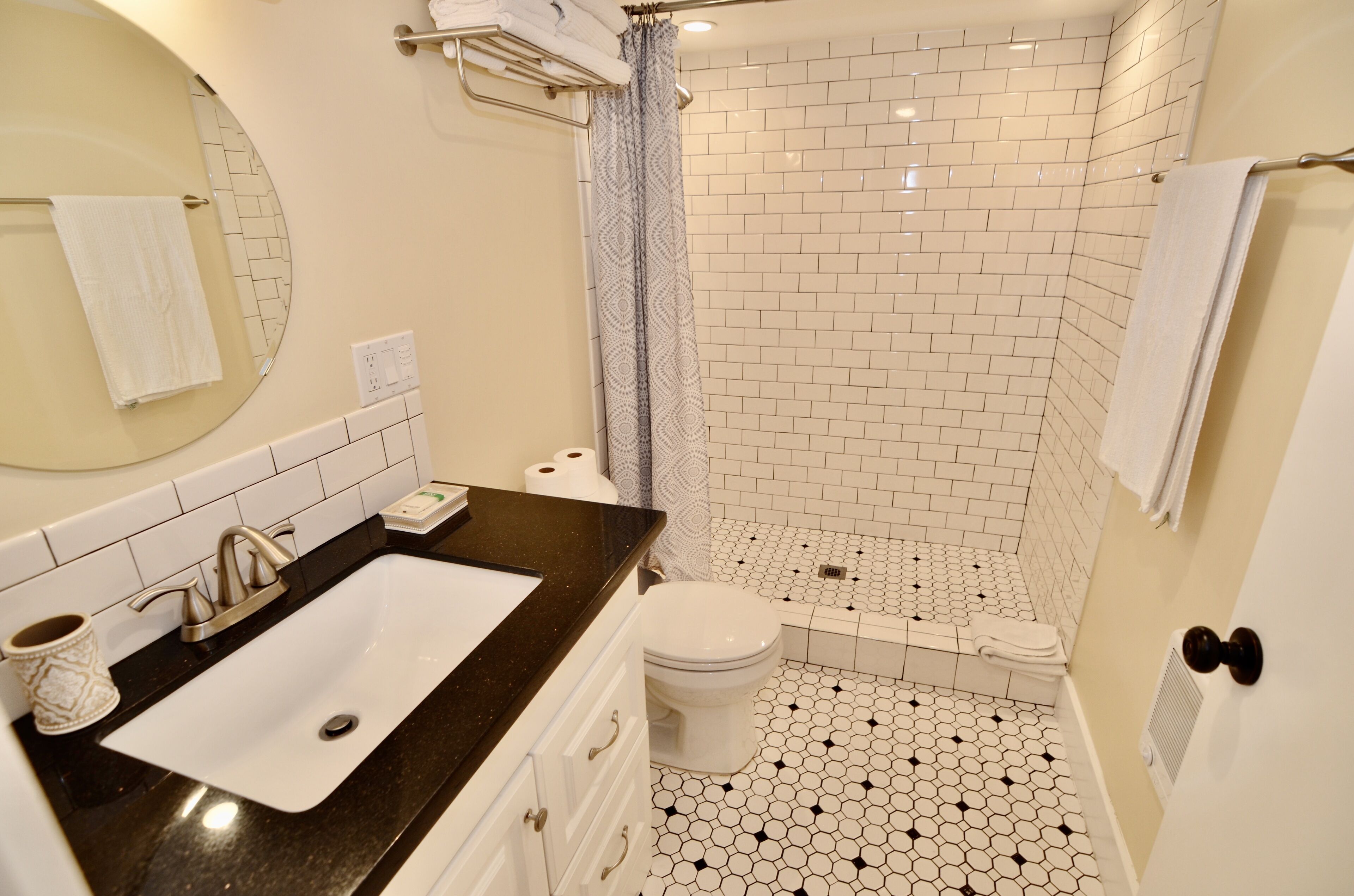 A bathroom with a black countertop sink, white toilet, and a shower area with white and black patterned tiles.