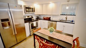 A compact kitchen with white cabinets, stainless steel appliances, and a dining area with a patterned tablecloth. - Modern Suite Nearby Convention Center (2bd, 1bth) (Portland)