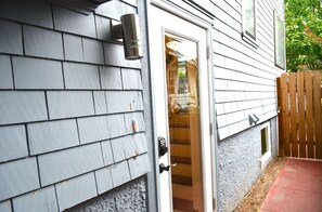 Ein Haus mit grauer Schindelfassade, einer weißen Tür mit Fensterglas und einem kleinen Fenster.