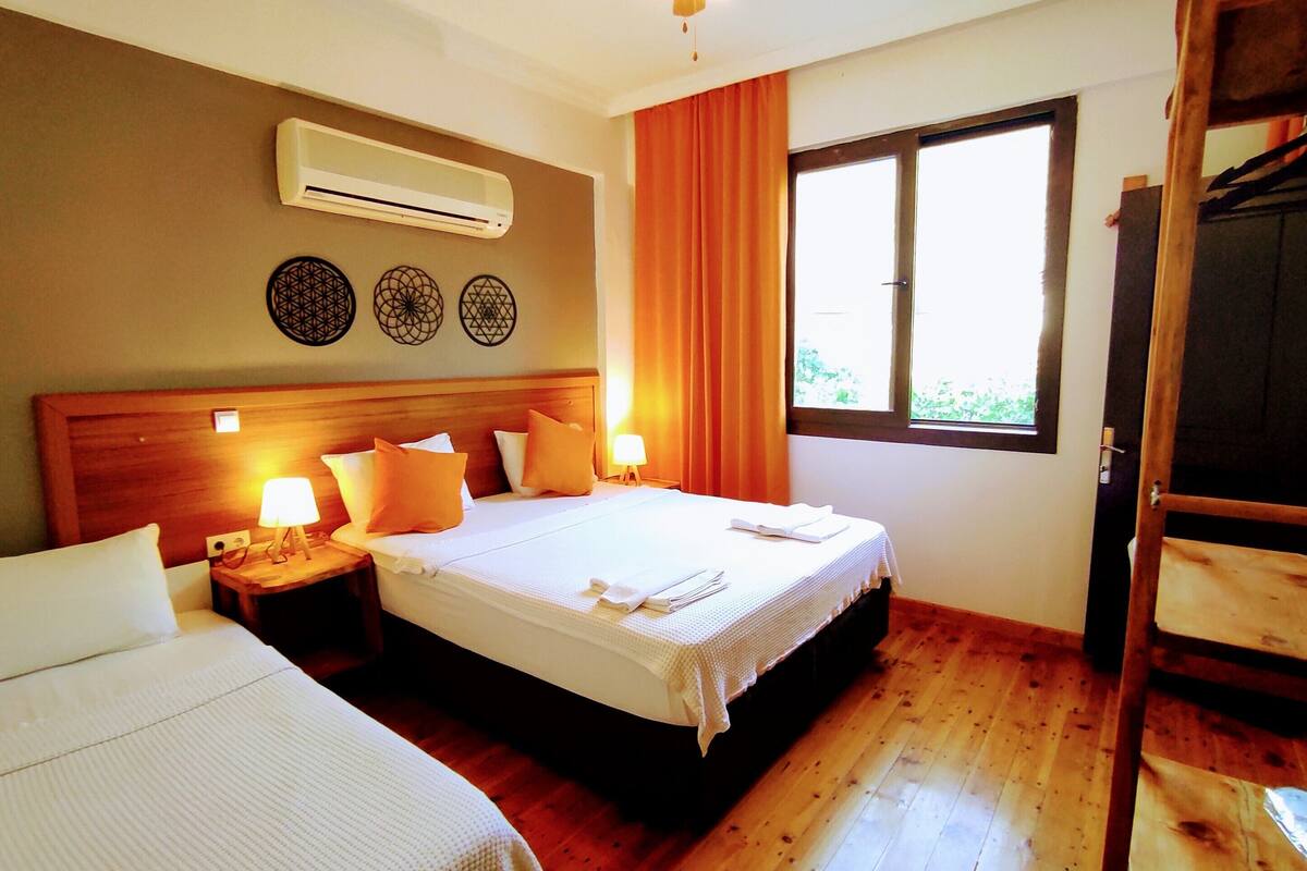 A hotel room with two beds, an air conditioner, decorative wall art, a window with curtains, and a ceiling fan.
