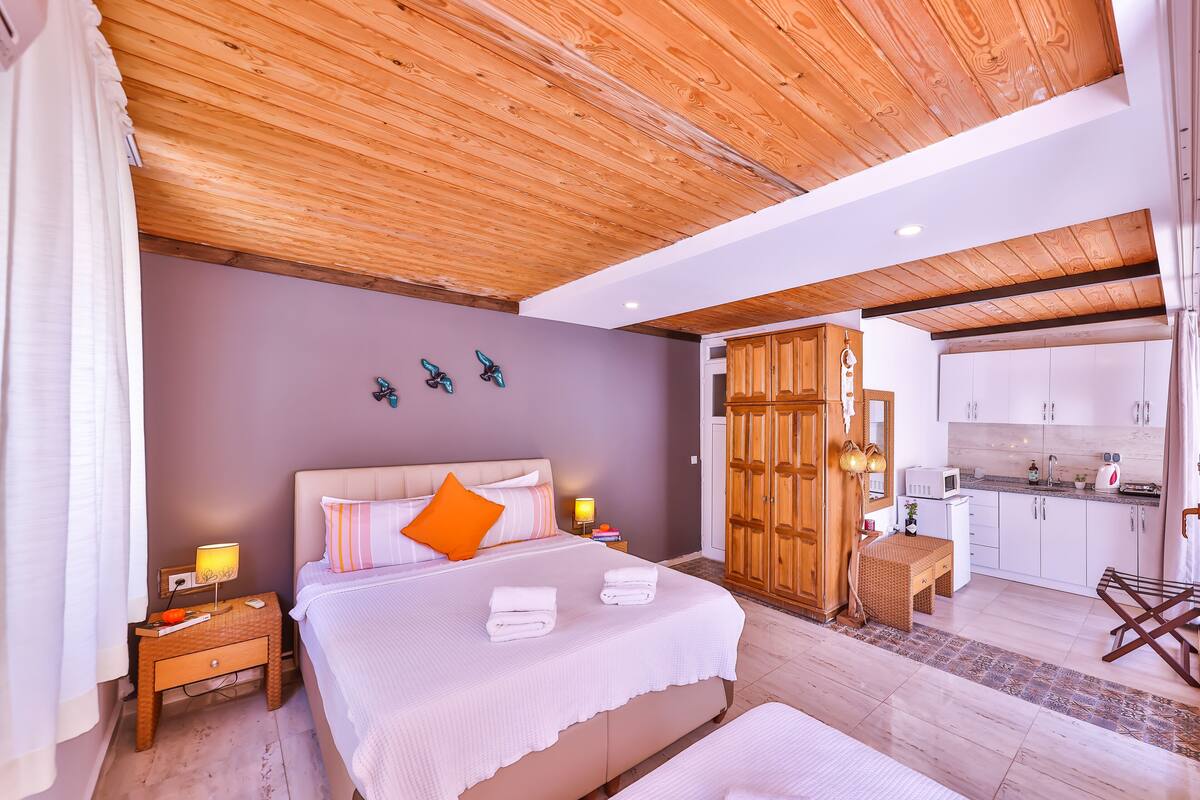A bedroom with a large bed, wooden wardrobe, and a view into the kitchen.