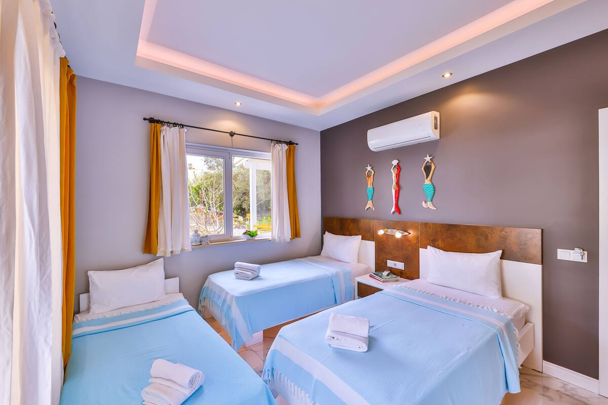 A hotel room with two beds, a window with curtains, an air conditioner, and a wall with decorative items.