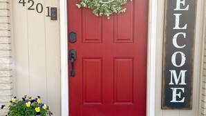A red door with a 'howdy' wreath, a 'WELCOME' sign, and a 'Welcome Friends' mat. - BCS Back Forty- fully stocked home & great yard—close to A&M, great food & fun. (Bryan)
