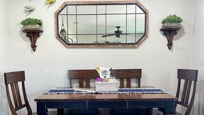 A dining room with a dark wooden table, white bench, and two wooden chairs. Above the table is a decorative mirror with a grid pattern. - BCS Back Forty- fully stocked home & great yard—close to A&M, great food & fun. (Bryan)