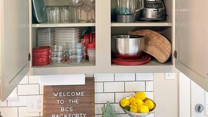 A kitchen with white cabinets, various dishes, a coffee maker, a blender, and a welcome sign. - BCS Back Forty- fully stocked home & great yard—close to A&M, great food & fun. (Bryan)