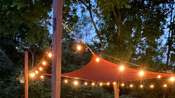 An outdoor patio area with a table and chairs, surrounded by a string of lights and a canopy. - BCS Back Forty- fully stocked home & great yard—close to A&M, great food & fun. (Bryan)