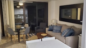 A modern living room with a sofa, chairs, a coffee table, and a dining area with a glass table and chairs. - Direct OceanFront, Modern, Clean, King Bed, Quartz Counters (Myrtle Beach)