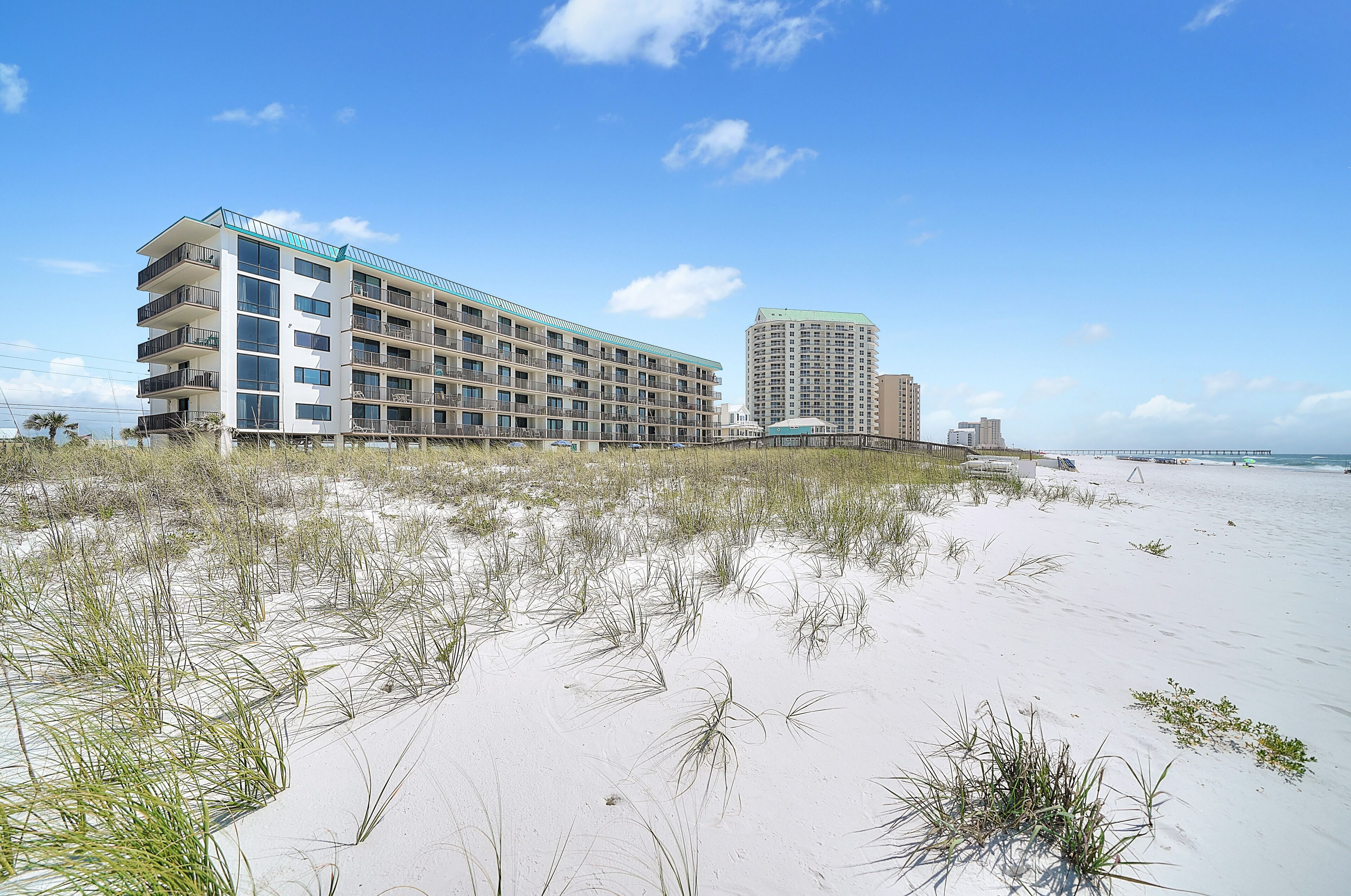 A beachfront hotel with multiple floors, a flat roof, and a sandy beach in the foreground.