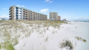 A beachfront hotel with multiple floors, a flat roof, and a sandy beach in the foreground. - Sunset Serenade-Gulf Front Unit with Community Pool (Navarre)