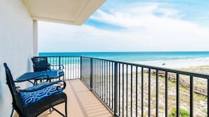 A balcony with two wicker chairs and a table, overlooking a beach with a clear view of the ocean and a sandy path leading to the water. - Sunset Serenade-Gulf Front Unit with Community Pool (Navarre)