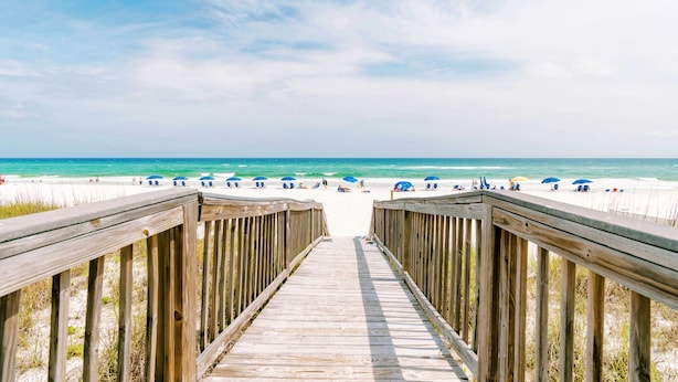 A wooden boardwalk leading to a beach with umbrellas and people. - Sunset Serenade-Gulf Front Unit with Community Pool (Navarre)