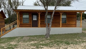 A log cabin with a front porch, a staircase, and a small tree in front. - 1 Bedroom Cabin w/Two Recliners Cabin 7  (Hamilton)