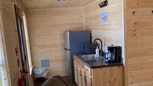 A compact kitchen with wooden walls, a refrigerator, a sink, and a coffee maker. - 1 Bedroom Cabin w/Two Recliners Cabin 7  (Hamilton)