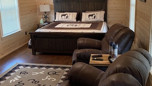 A cozy room with a wooden bed, a leather chair, and a small table with a lamp. - 1 Bedroom Cabin w/Two Recliners Cabin 7  (Hamilton)