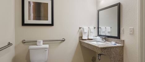 A bathroom with a toilet, sink, and mirror. There is a framed picture on the wall and a towel rack with towels.