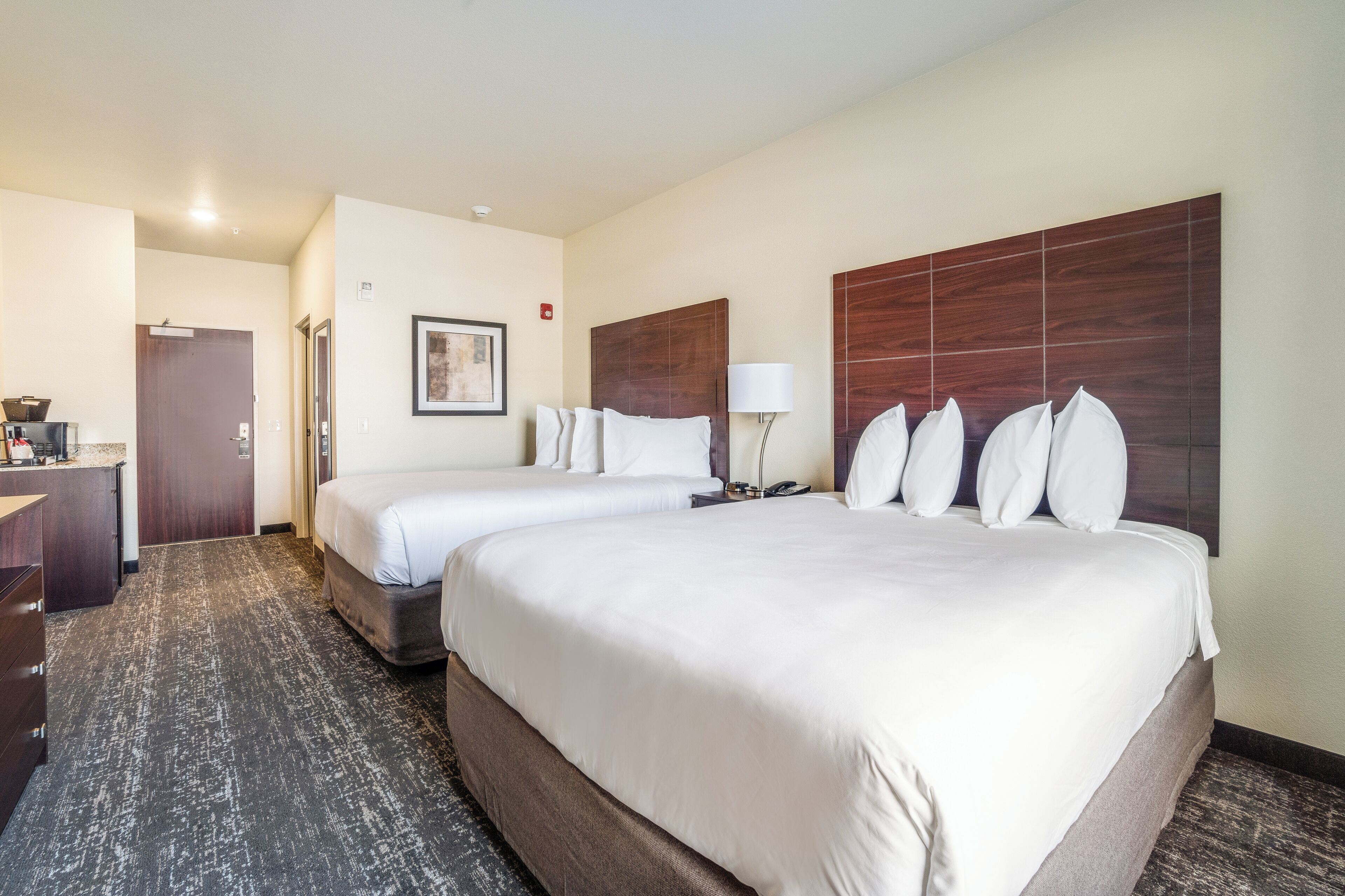 A hotel room with two beds, a desk, a chair, a lamp, and a framed picture on the wall.