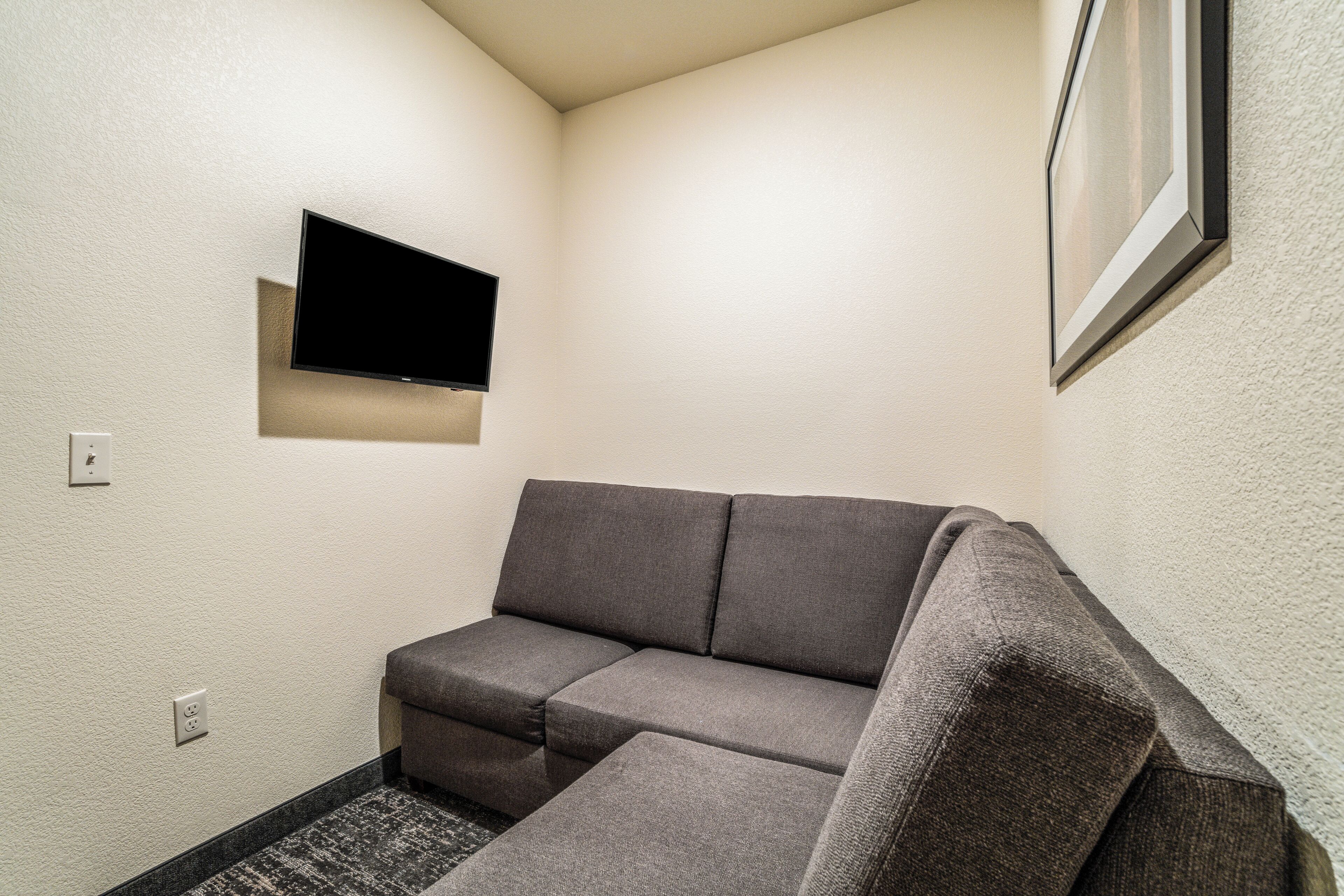 Ein Eckzimmer mit grauem Sofa, einem flachbildfernseher an der Wand und einem gerahmten Bild über dem Sofa.