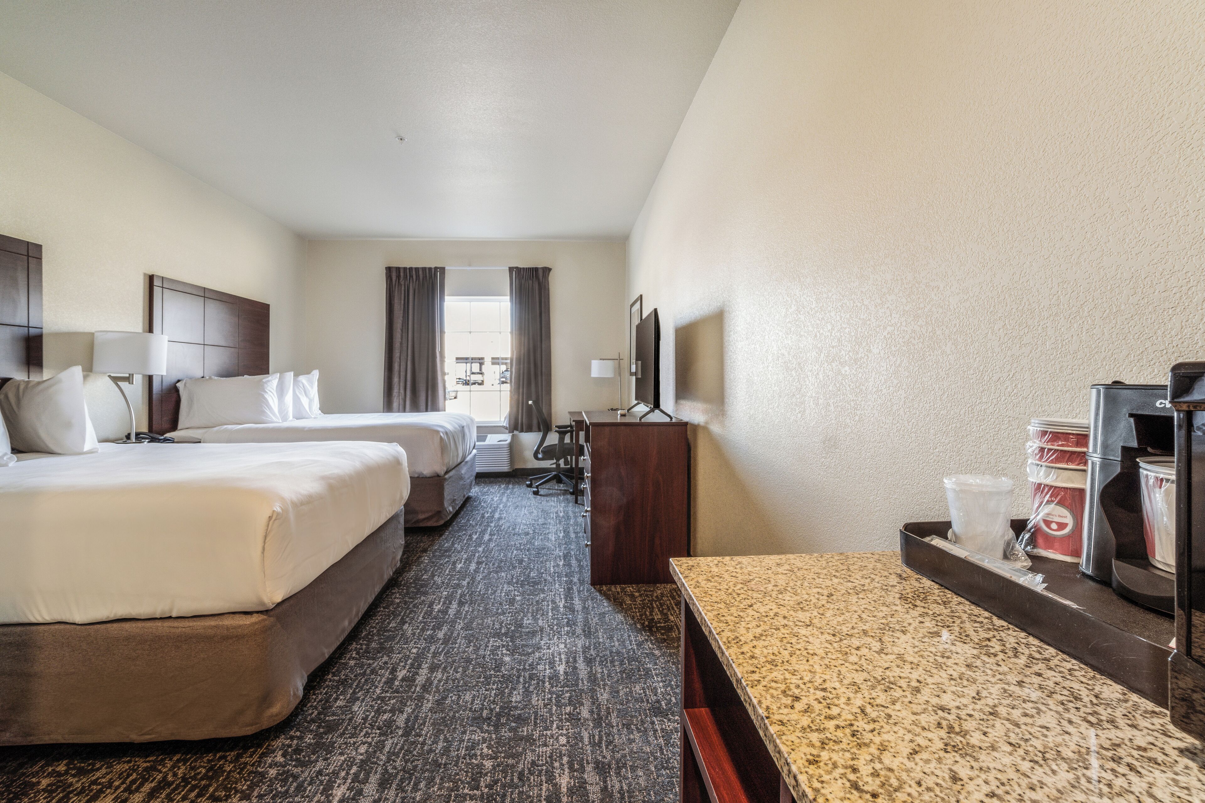 A hotel room with two beds, a desk, a chair, a TV, and a window with curtains.