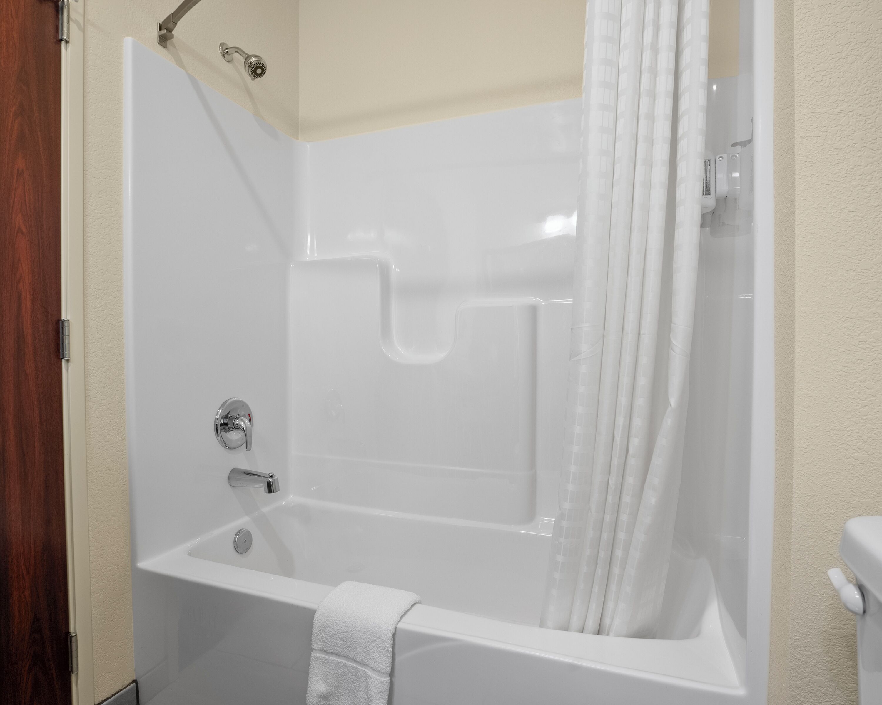 Una bañera blanca con cortina de ducha, una toalla y un cabezal de ducha.