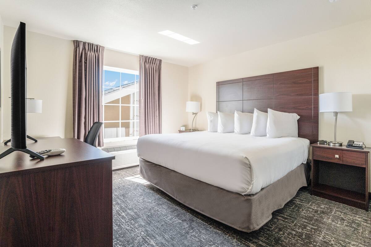 Ein Hotelzimmer mit einem großen Bett, einem Schreibtisch mit Fernseher und einem Fenster mit Vorhängen.