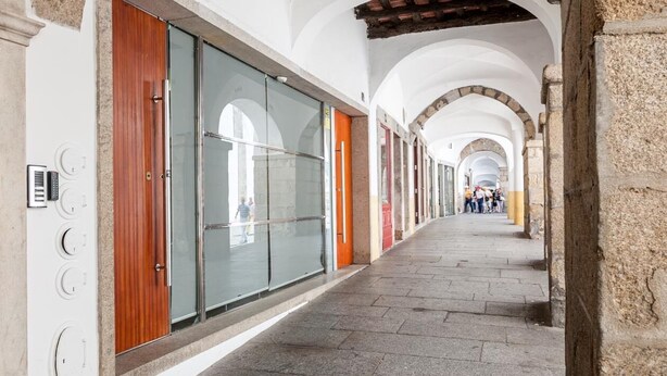 Un corridoio con archi, pavimento piastrellato e una fila di negozi con vetrine e porte in legno.