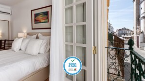 Una camera d'albergo con un letto, un quadro appeso alla parete e vista sulla città da una porta aperta.