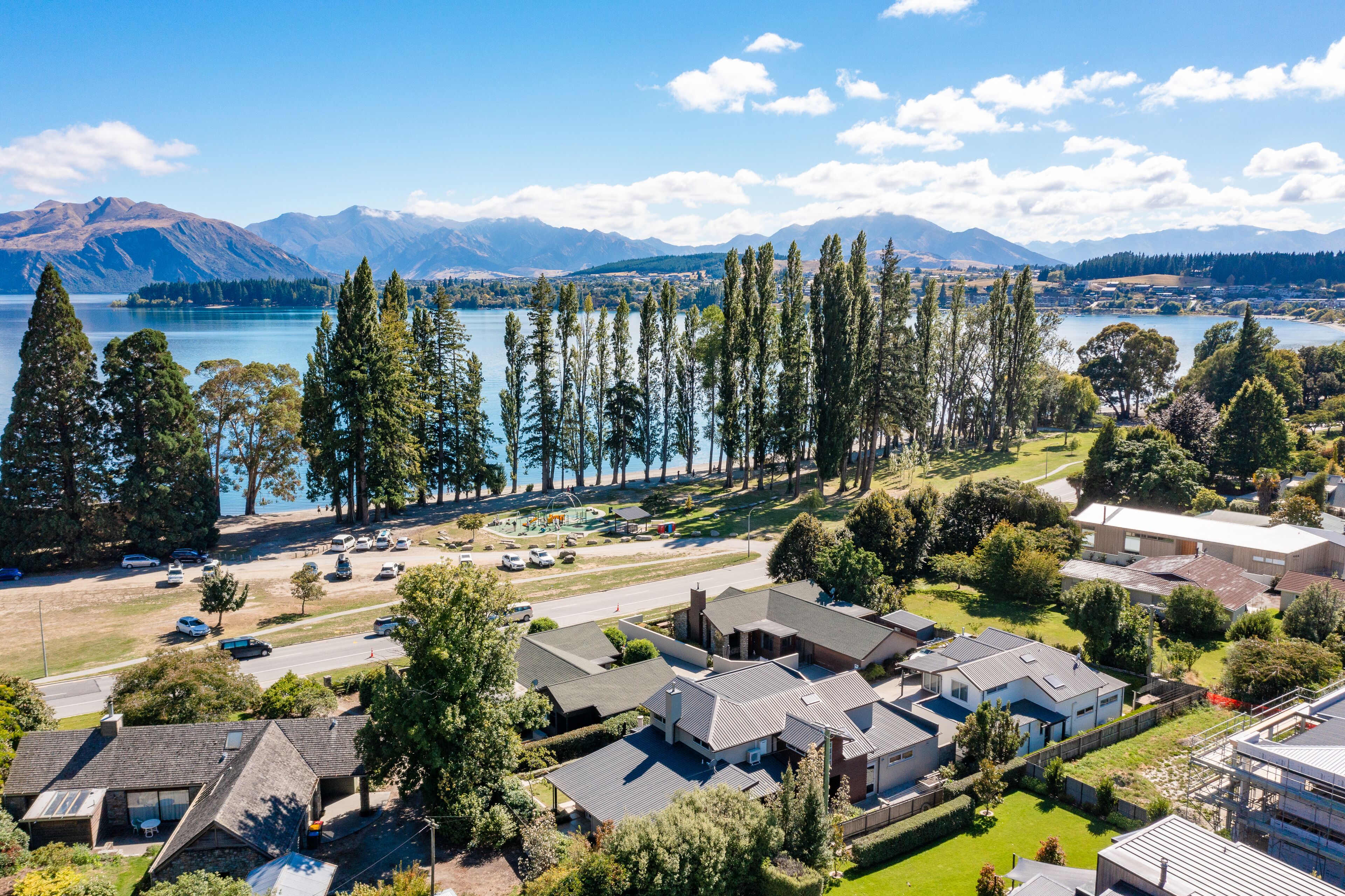 A residential area with houses, a road, and a lake with mountains in the background.