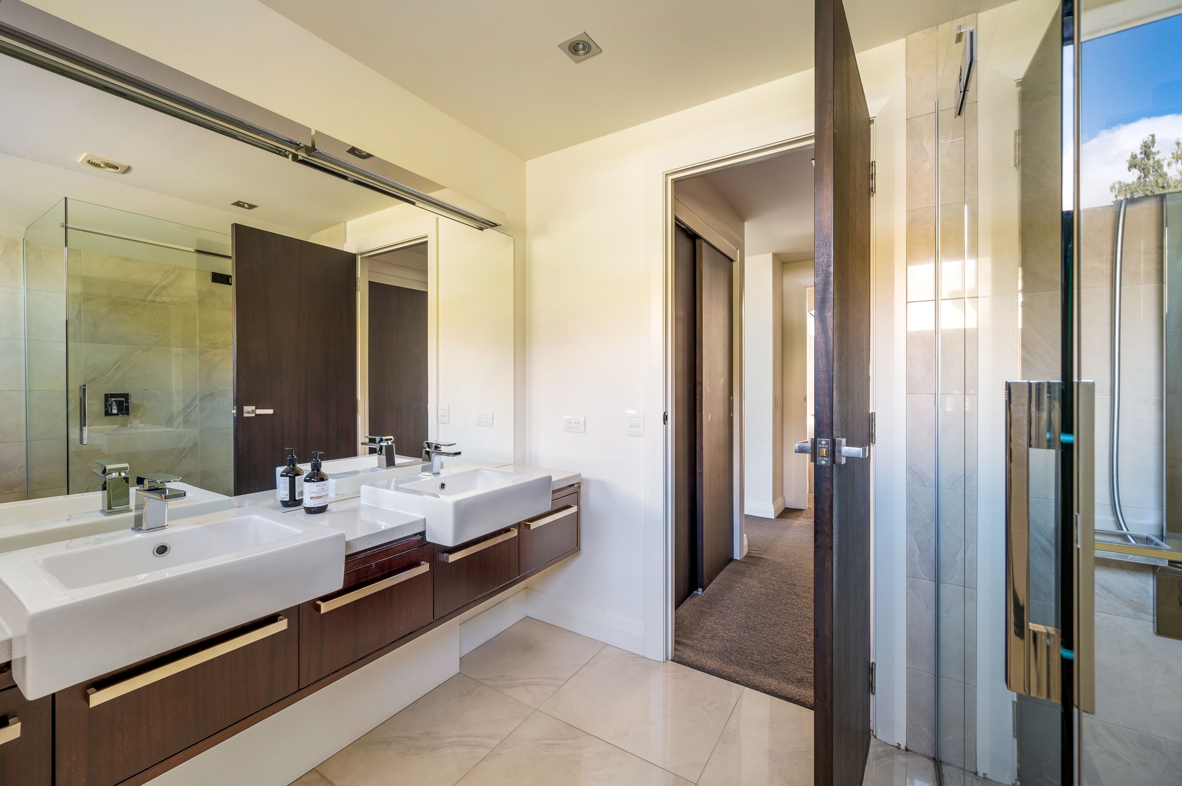 Un bagno moderno con due lavandini, uno specchio grande e una cabina doccia.