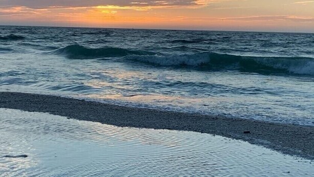 A beach with waves and a sunset.