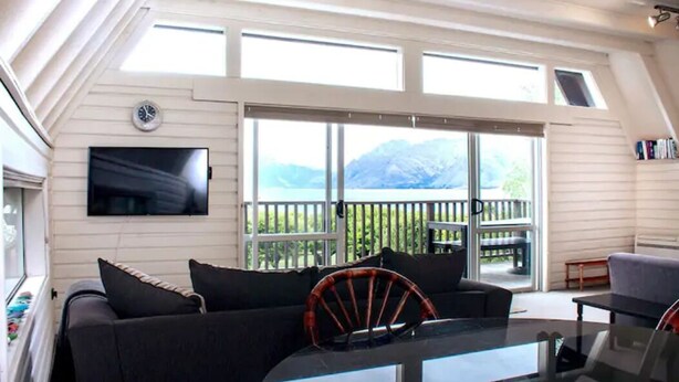 Un soggiorno moderno con una grande TV, un divano e un tavolo da pranzo. Sul balcone, vista sulle montagne.