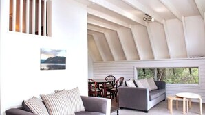 Un interno moderno con soffitto alto, una zona pranzo con sedie di legno e un divano grigio.