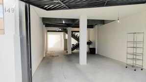 Un interior amplio y moderno, con techos a la vista, pisos de concreto y una estantería metálica.