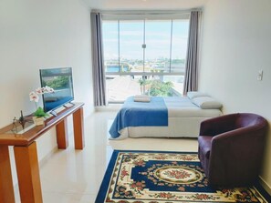 A hotel room with a bed, a desk with a television, a chair, and a large window with a city view. - Sky S House (São Paulo)