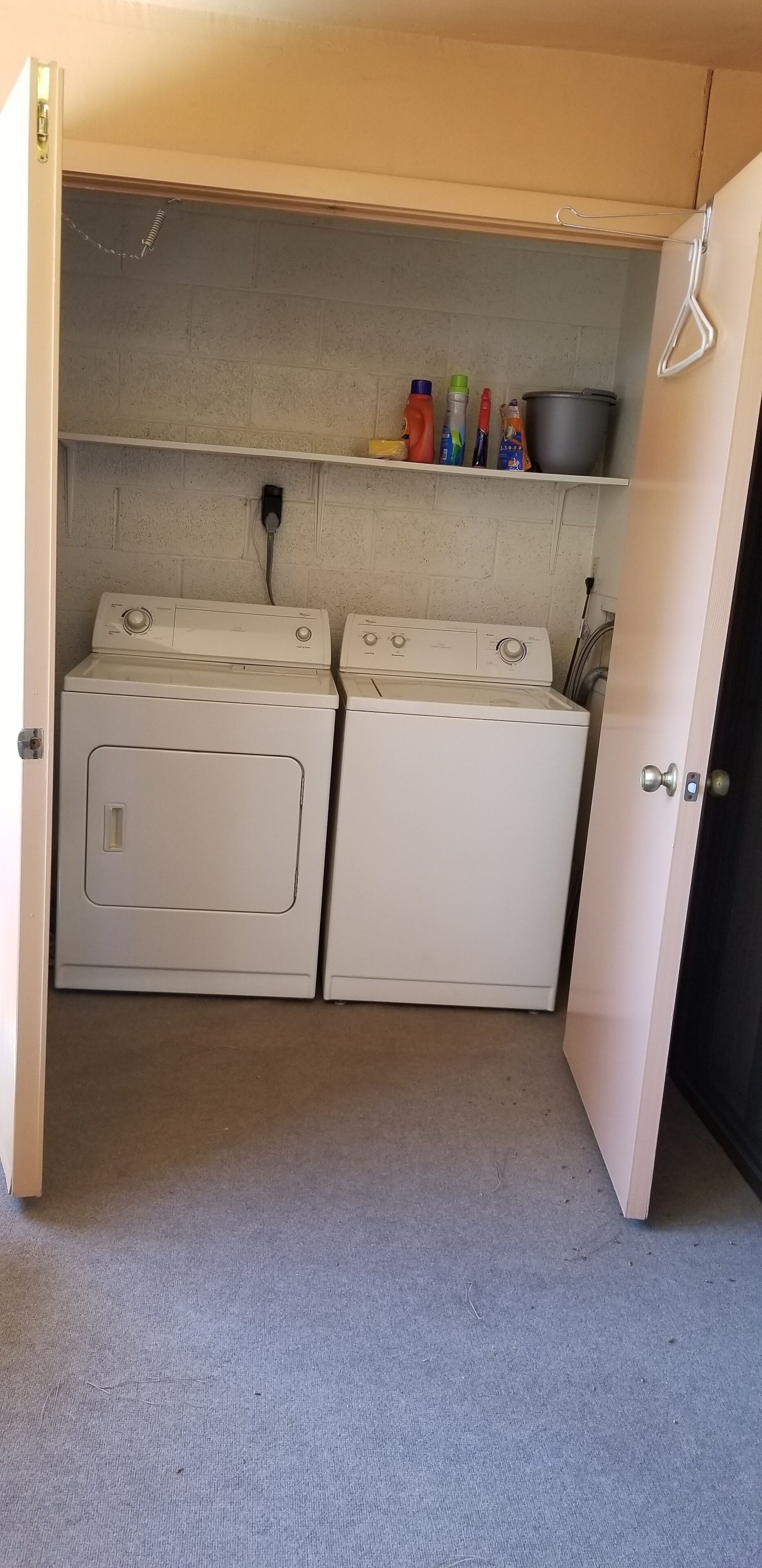 A laundry area with two white washing machines and a shelf above containing cleaning supplies.