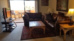 A living room with a brown leather sofa, a wooden coffee table, a TV on a stand, a lamp, and a view of the outside balcony. - Cozy 1 bedroom/1 Bathroom with large living room & kitchen. (Phoenix)