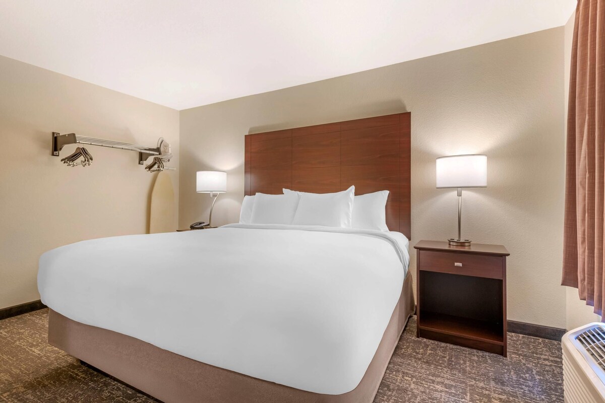 A hotel room with a large bed, two bedside tables with lamps, a wall-mounted coat rack, and a wooden headboard.