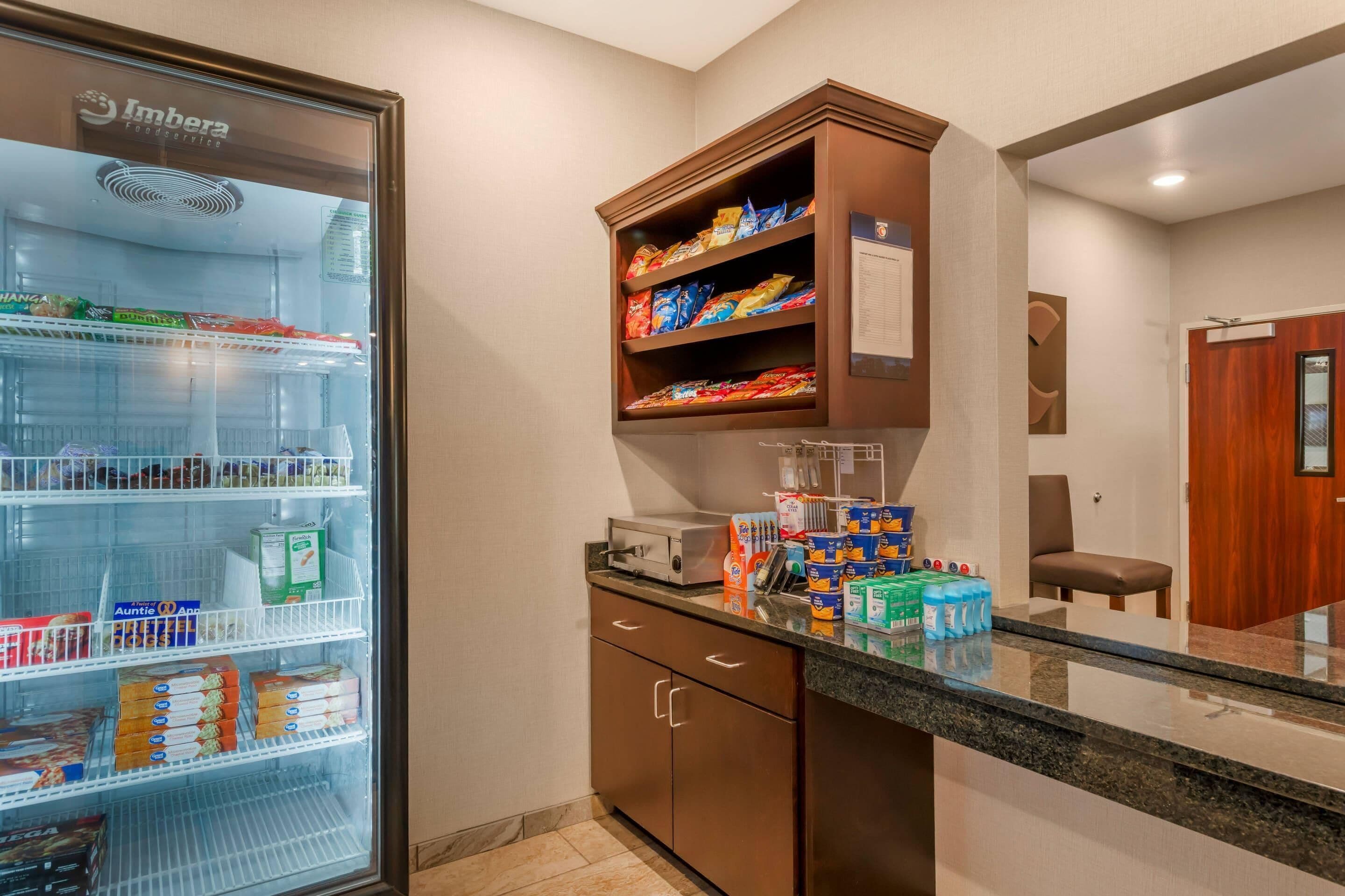 A kitchenette with a refrigerator stocked with beverages, a microwave, and various food items on shelves.
