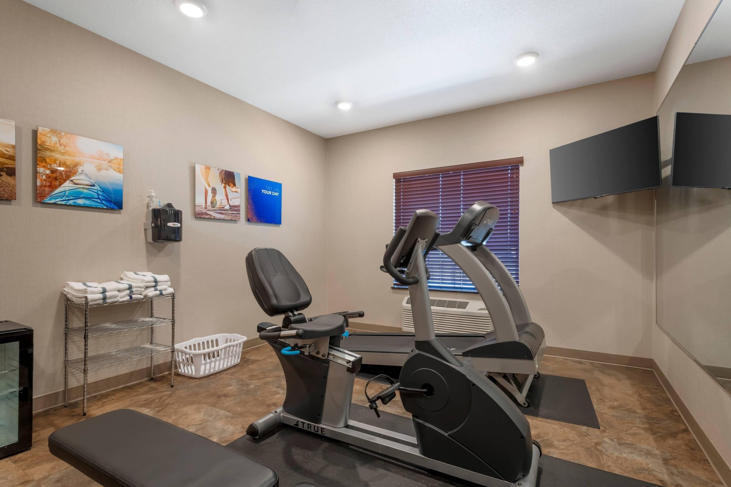 Un gimnasio con equipo de ejercicio, un televisor y obras de arte en las paredes.