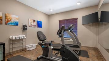 Un gimnasio con equipo de ejercicio, un televisor y obras de arte en las paredes.