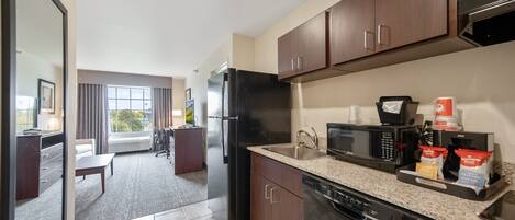 A modern kitchen with dark wooden cabinets, a stainless steel refrigerator, a microwave, and a dishwasher. There is a window providing natural light and a view of the outdoors.