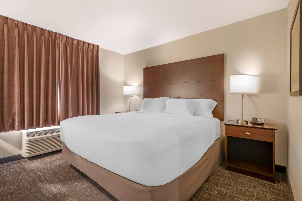 Habitación de hotel con una cama grande, dos mesitas de noche con lámparas, una ventana con cortinas y un aire acondicionado instalado en la pared.
